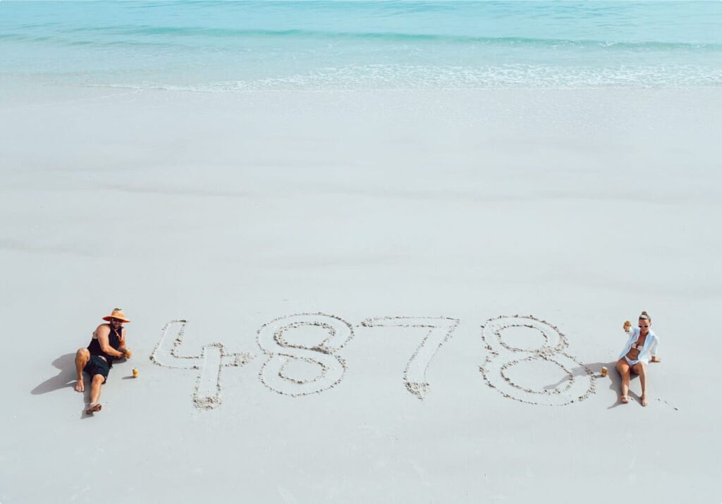 Two people on a beautiful QLD beach with "4878" written in the sand